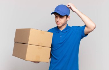 Genç paket teslim çocuk şaşkın ve kafası karışık hissediyor, başını kaşıyor ve yan bakıyor