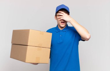 Genç teslimatçı çocuk şok olmuş, korkmuş ya da korkmuş görünüyordu. Yüzü elle kaplıydı ve parmaklarının arasından bakıyordu.