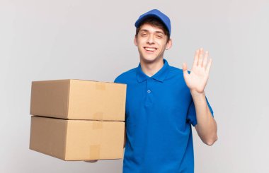 Genç paket teslimatçısı, mutlu ve neşeli bir şekilde gülümseyen, el sallayan, seni selamlayan, ya da hoşça kal diyen