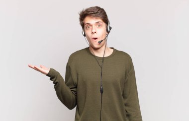 Genç tele pazarlamacı şaşırmış ve şok olmuş görünüyor. Çenesi düşmüş ve eli açık bir nesneyi tutuyor.