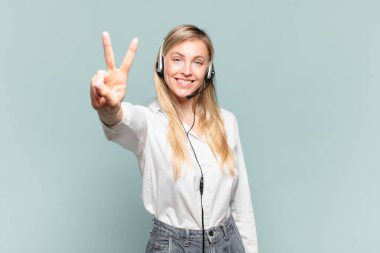 Genç sarışın tele pazarlamacı kadın gülümsüyor ve mutlu görünüyor, kaygısız ve pozitif, zafer ya da barışı simgeliyor.