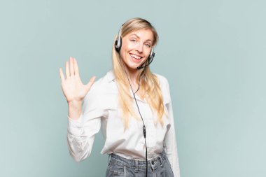 Genç sarışın tele pazarlamacı kadın mutlu ve neşeli bir şekilde gülümsüyor, el sallıyor, seni selamlıyor ya da veda ediyor.