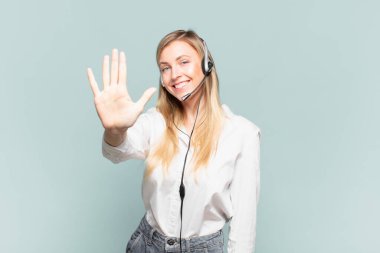 Genç sarışın tele pazarlamacı kadın gülümsüyor ve arkadaş canlısı görünüyor, 5 ya da 5 numarayı gösteriyor, eli önde, geri sayıyor.