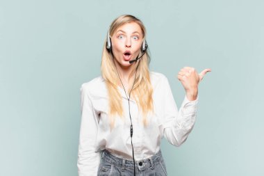 Genç sarışın tele pazarlamacı kadın inançsızlıktan şaşkın şaşkın bakıyor, yan taraftaki objeyi işaret ediyor ve diyor ki: