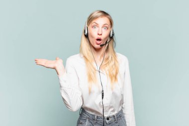 Genç sarışın tele-pazarlamacı kadın şaşırmış ve şok olmuş görünüyor, çenesi düşmüş, elinde açık bir elle bir nesne tutuyor.