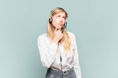 Genç sarışın tele pazarlamacı kadın düşünüyor, kuşkulu ve şaşkın hissediyor, farklı seçeneklerle, hangi kararı vereceğini merak ediyor.