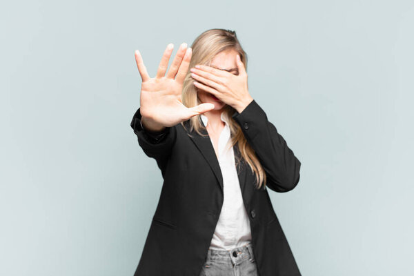 young pretty businesswoman covering face with hand and putting other hand up front to stop camera, refusing photos or pictures