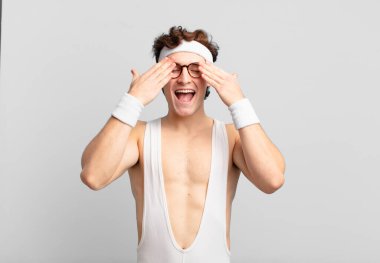 humorous sport man smiling and feeling happy, covering eyes with both hands and waiting for unbelievable surprise