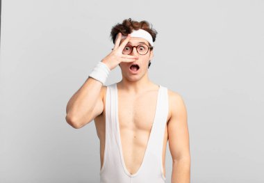 humorous sport man looking shocked, scared or terrified, covering face with hand and peeking between fingers
