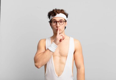 humorous sport man looking serious and cross with finger pressed to lips demanding silence or quiet, keeping a secret