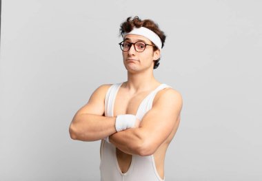 humorous sport man shrugging, feeling confused and uncertain, doubting with arms crossed and puzzled look