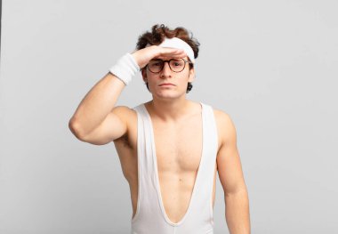 humorous sport man looking bewildered and astonished, with hand over forehead looking far away, watching or searching