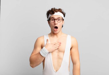 humorous sport man feeling shocked, astonished and surprised, with hand on chest and open mouth, saying who, me?