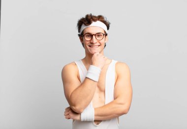 humorous sport man smiling, enjoying life, feeling happy, friendly, satisfied and carefree with hand on chin