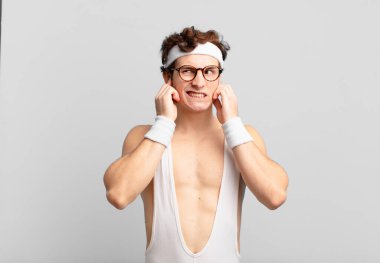 humorous sport man looking angry, stressed and annoyed, covering both ears to a deafening noise, sound or loud music