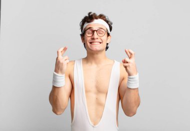 humorous sport man smiling and anxiously crossing both fingers, feeling worried and wishing or hoping for good luck