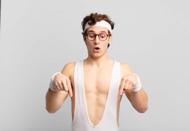 humorous sport man with open mouth pointing downwards with both hands, looking shocked, amazed and surprised