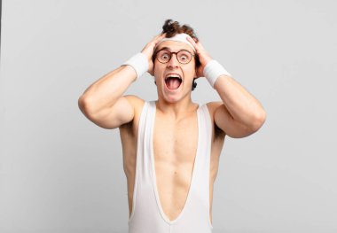 humorous sport man raising hands to head, open-mouthed, feeling extremely lucky, surprised, excited and happy