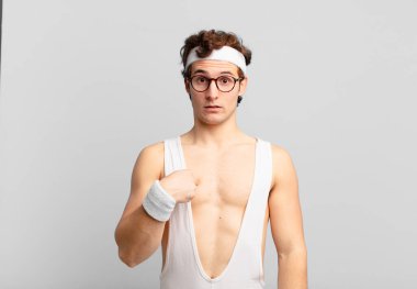 humorous sport man feeling confused, puzzled and insecure, pointing to self wondering and asking who, me?