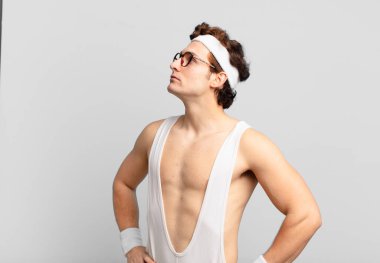 humorous sport man feeling confused or full or doubts and questions, wondering, with hands on hips, rear view