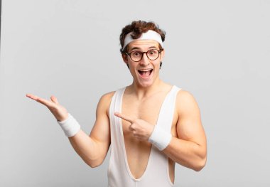 humorous sport man smiling cheerfully and pointing to copy space on palm on the side, showing or advertising an object