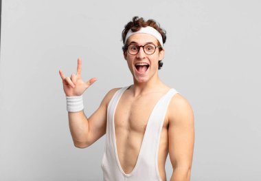 humorous sport man feeling happy, fun, confident, positive and rebellious, making rock or heavy metal sign with hand