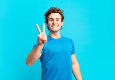 young sport boy smiling and looking happy, carefree and positive, gesturing victory or peace with one hand