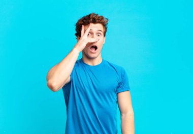 young sport boy looking shocked, scared or terrified, covering face with hand and peeking between fingers