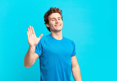 young sport boy smiling happily and cheerfully, waving hand, welcoming and greeting you, or saying goodbye