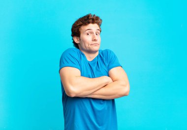 young sport boy shrugging, feeling confused and uncertain, doubting with arms crossed and puzzled look