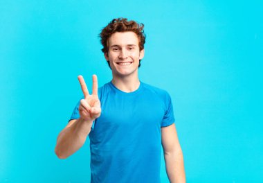 Genç sporcu çocuk gülümsüyor ve arkadaş canlısı görünüyor, iki ya da iki numarayı gösteriyor, elleri önde, geriye doğru sayıyor.