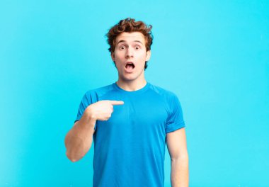 Genç sporcu çocuk şok olmuş ve ağzı açık, kendini işaret ederek şaşırmış görünüyor.