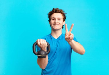 Genç sporcu çocuk gülümsüyor ve mutlu görünüyor, kaygısız ve pozitif, tek elle zafer ya da barış işareti yapıyor. dambıl konsepti