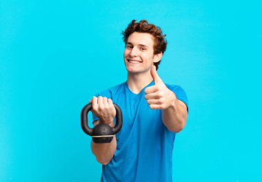 Genç sporcu çocuk kendini gururlu, tasasız, kendinden emin ve mutlu hissediyor. Başparmağıyla olumlu gülümsüyor. dambıl konsepti