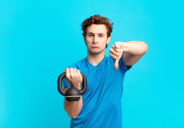 Genç sporcu çocuk kızgın, sinirli, hayal kırıklığına uğramış ya da canı sıkkın, ciddi bir bakışla baş parmağını aşağı gösteriyor. dambıl konsepti