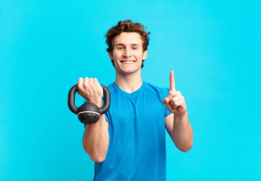 Genç sporcu çocuk gülümsüyor ve arkadaş canlısı görünüyor, bir numara ya da ilk eli önde, geriye doğru sayıyor. dambıl konsepti