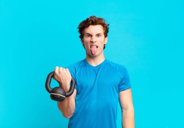 young sport boy feeling disgusted and irritated, sticking tongue out, disliking something nasty and yucky. dumbbell concept
