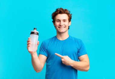 sport boy smiling cheerfully, feeling happy and pointing to the side and upwards, showing object in copy space. energy drink concept clipart