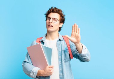 Genç öğrenci mutlu ve neşeli bir şekilde gülümsüyor, el sallıyor, sizi selamlıyor ve selamlıyor, ya da veda ediyor.