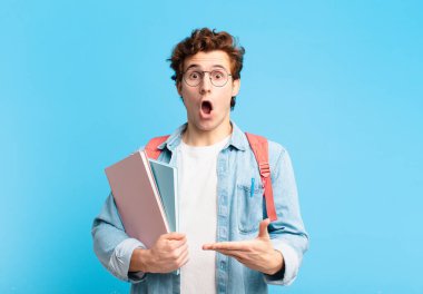 Genç öğrenci şaşırmış ve şoka uğramış görünüyor, çenesi düşmüş ve eli açık bir nesneyi tutuyor.