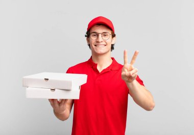 Pizza dağıtan çocuk gülümsüyor ve mutlu görünüyor, kaygısız ve pozitif, zafer veya barış işareti yapıyor.