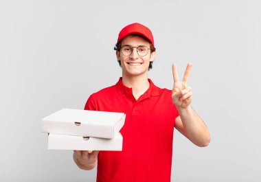 Pizza dağıtan çocuk gülümsüyor ve arkadaş canlısı görünüyor. İki ya da iki numarayı gösteriyor. Elleri önde, geriye doğru sayıyor.