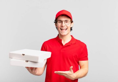 Pizza dağıtan çocuk mutlu bir şekilde gülümsüyor, kendini mutlu hissediyor ve fotokopi uzayında bir konsept gösteriyor.