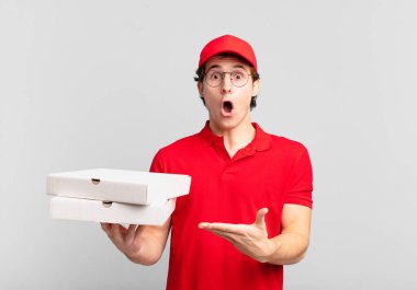 Pizza teslimatçısı çocuk şaşırmış ve şok olmuş görünüyor, çenesi düşmüş, bir objeyi elinde açık bir elle tutuyor.