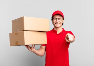 Paket teslimatçısı çocuk kameraya bakıyor, kendinden emin, arkadaş canlısı bir gülümsemeyle, seni seçiyor.