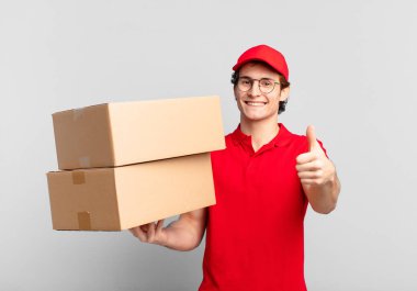 Paket teslimatçısı gururlu, kaygısız, kendinden emin ve mutlu, başparmağıyla olumlu gülümseyen