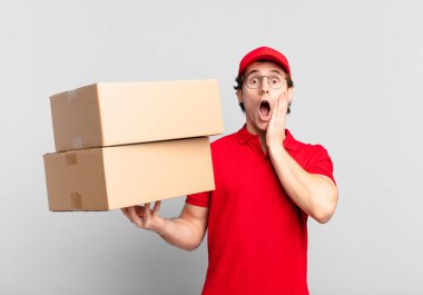 Paket teslimatçısı şok olmuş ve korkmuş hissediyor, ağzı açık ve elleri yanaklarında korkmuş görünüyor.