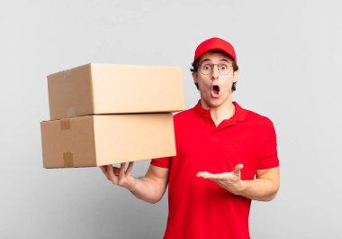 Paket teslimatçısı çocuk şaşırmış ve şok olmuş görünüyor, çenesi düşmüş bir nesneyi elinde açık bir elle tutuyor.