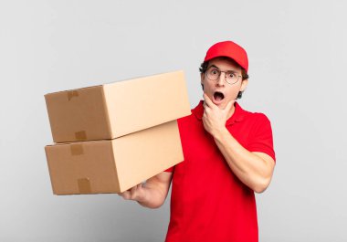 Paket teslimatçısı çocuk ağzı ve gözleri sonuna kadar açık ve elleri çenesinde, nahoş bir şok hissediyor, ne söylüyor veya vay be