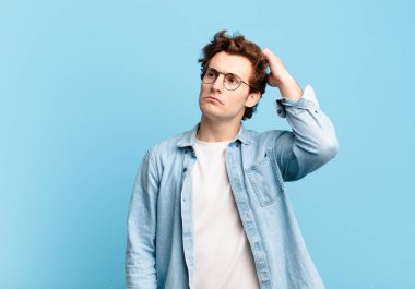 Genç yakışıklı çocuk şaşkın ve kafası karışmış hissediyor, başını kaşıyor ve yan tarafa bakıyor.